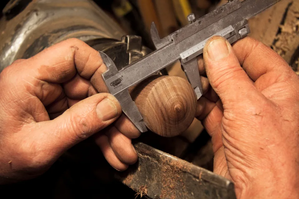 A craftsman measuring a turned wood detail with calipers